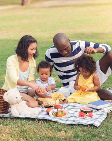 A group of friends are hugging and laughing together in a sunny outdoor setting.