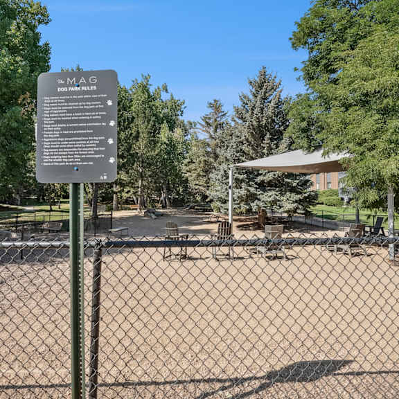 A sign in a park with a fence in the foreground.