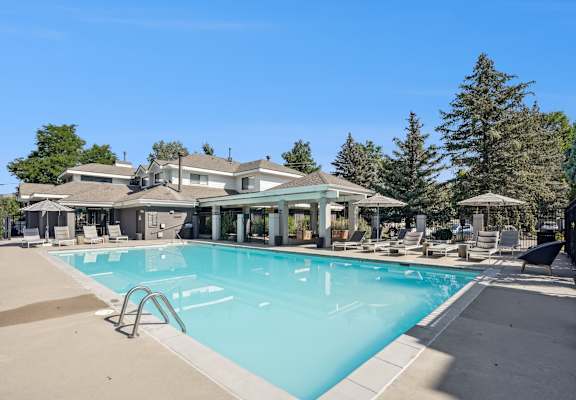 A large swimming pool in front of a house with a patio and trees in the background.