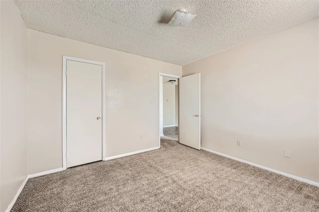 Empty bedroom with two doors and plush carpeting.