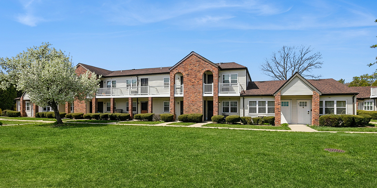 Charming brick apartment complex with lush green lawn and beautiful blue sky backdrop, offering serene and comfortable living.