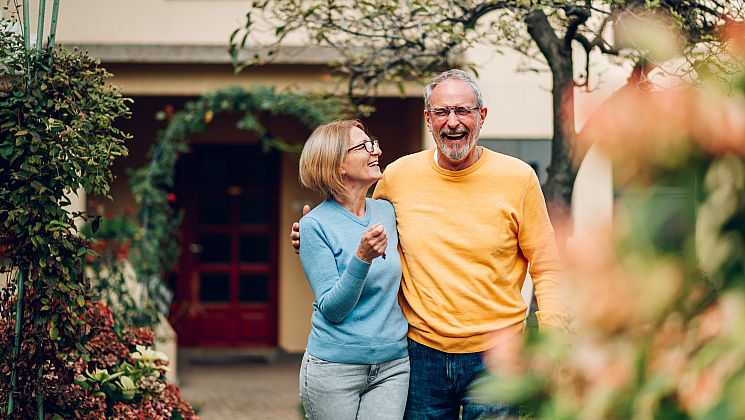 Joyful couple enjoying a sunny day in a beautifully landscaped garden, showcasing vibrant plants and an inviting home entrance.