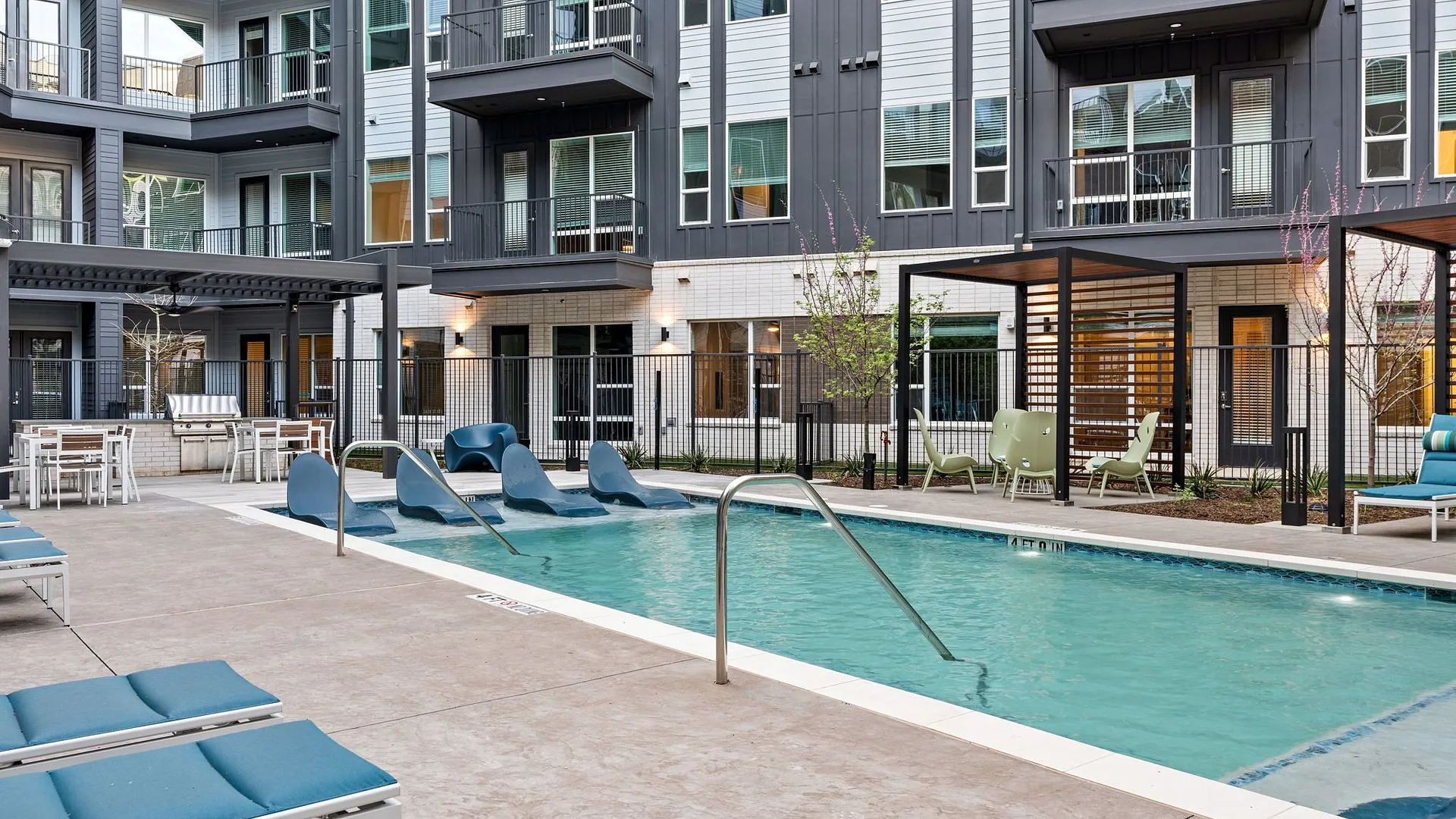 A modern apartment complex with a pool, lounge chairs, and landscaped areas.