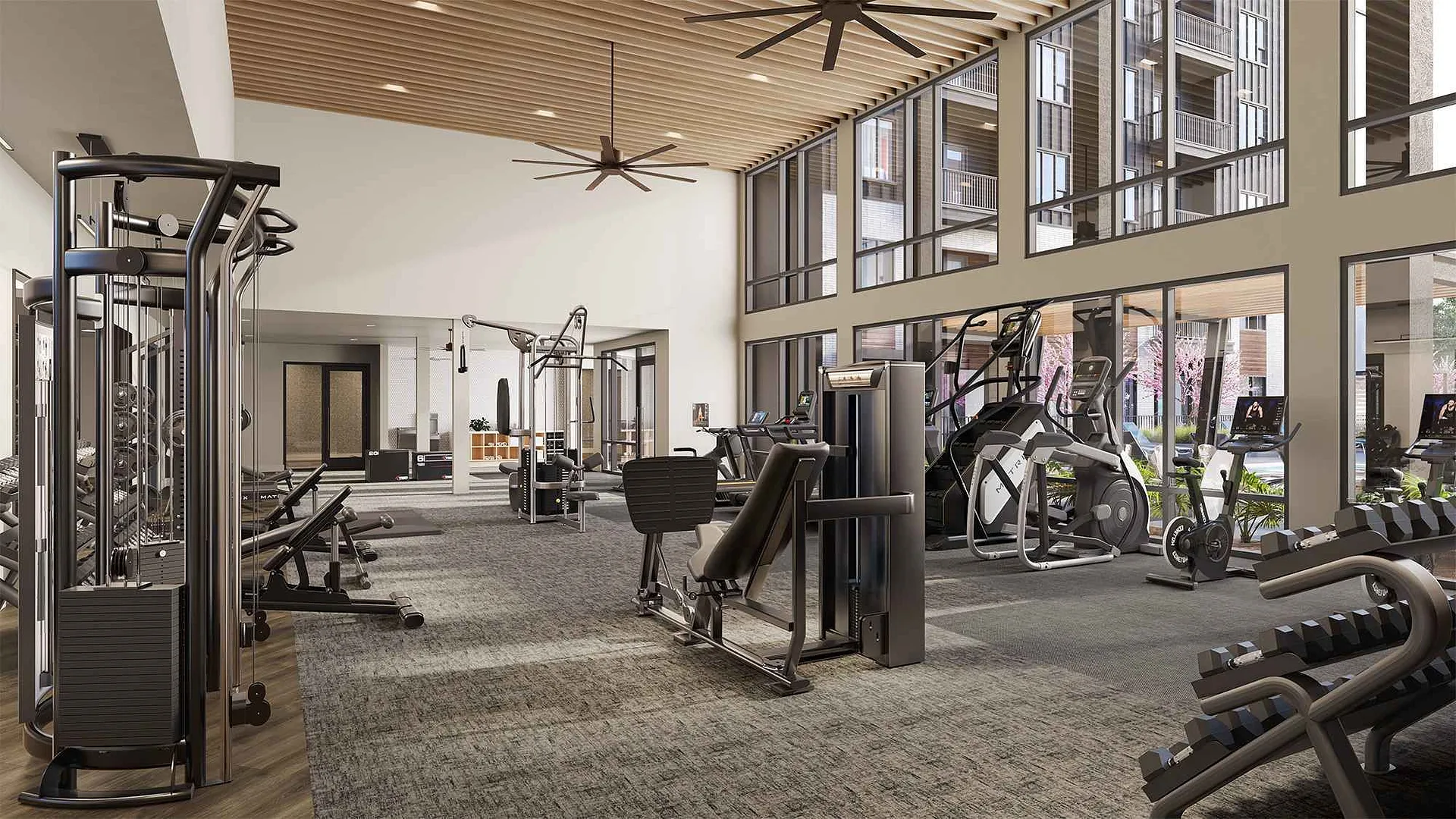 A modern gym with various workout equipment and large windows letting in natural light.