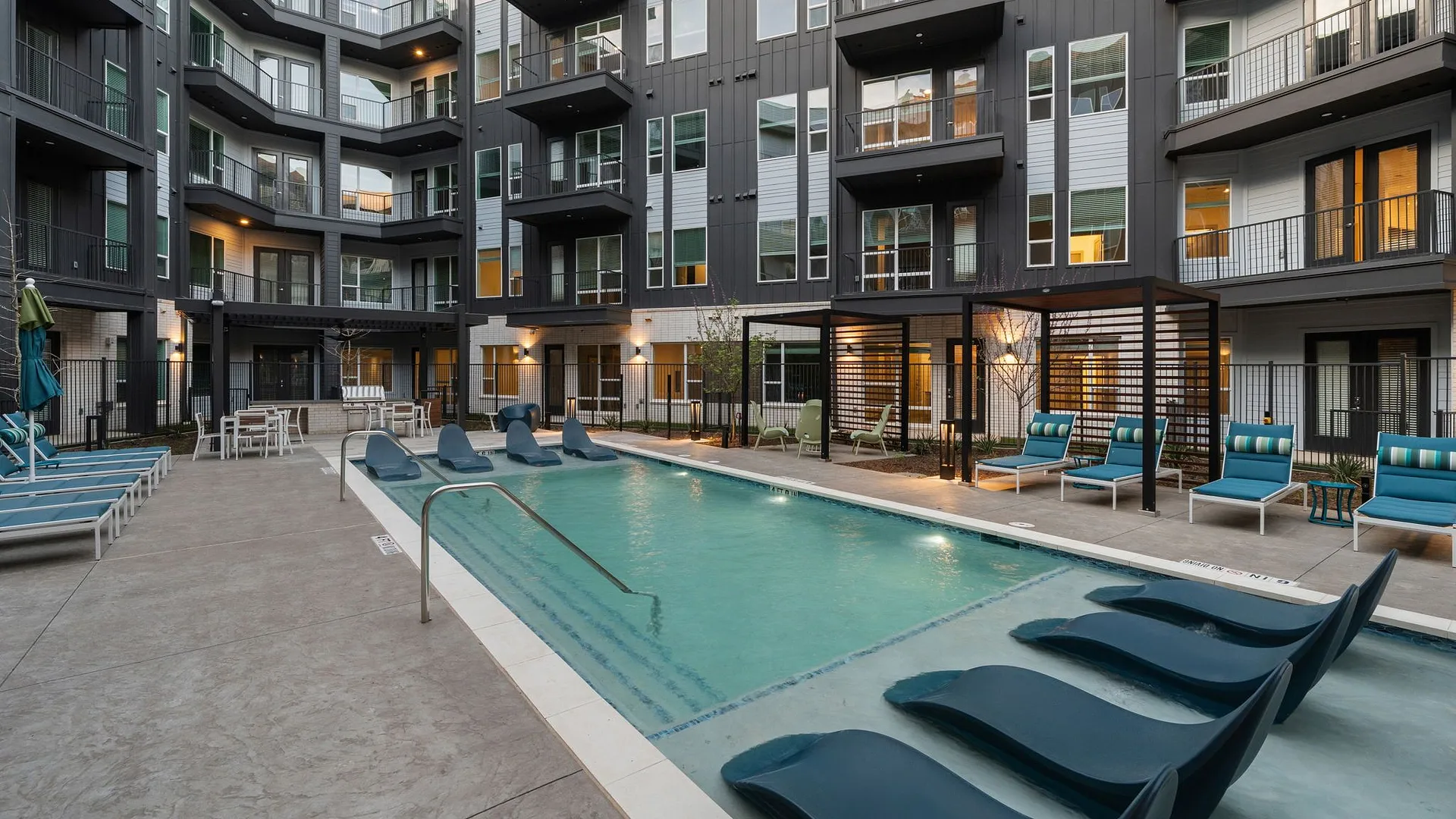 Modern apartment complex with a pool and lounge chairs.