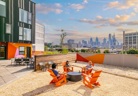 A group of people are sitting on orange chairs on a rooftop terrace.