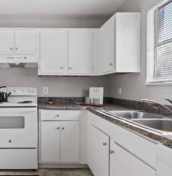 A white kitchen with a stove, sink, and cabinets.