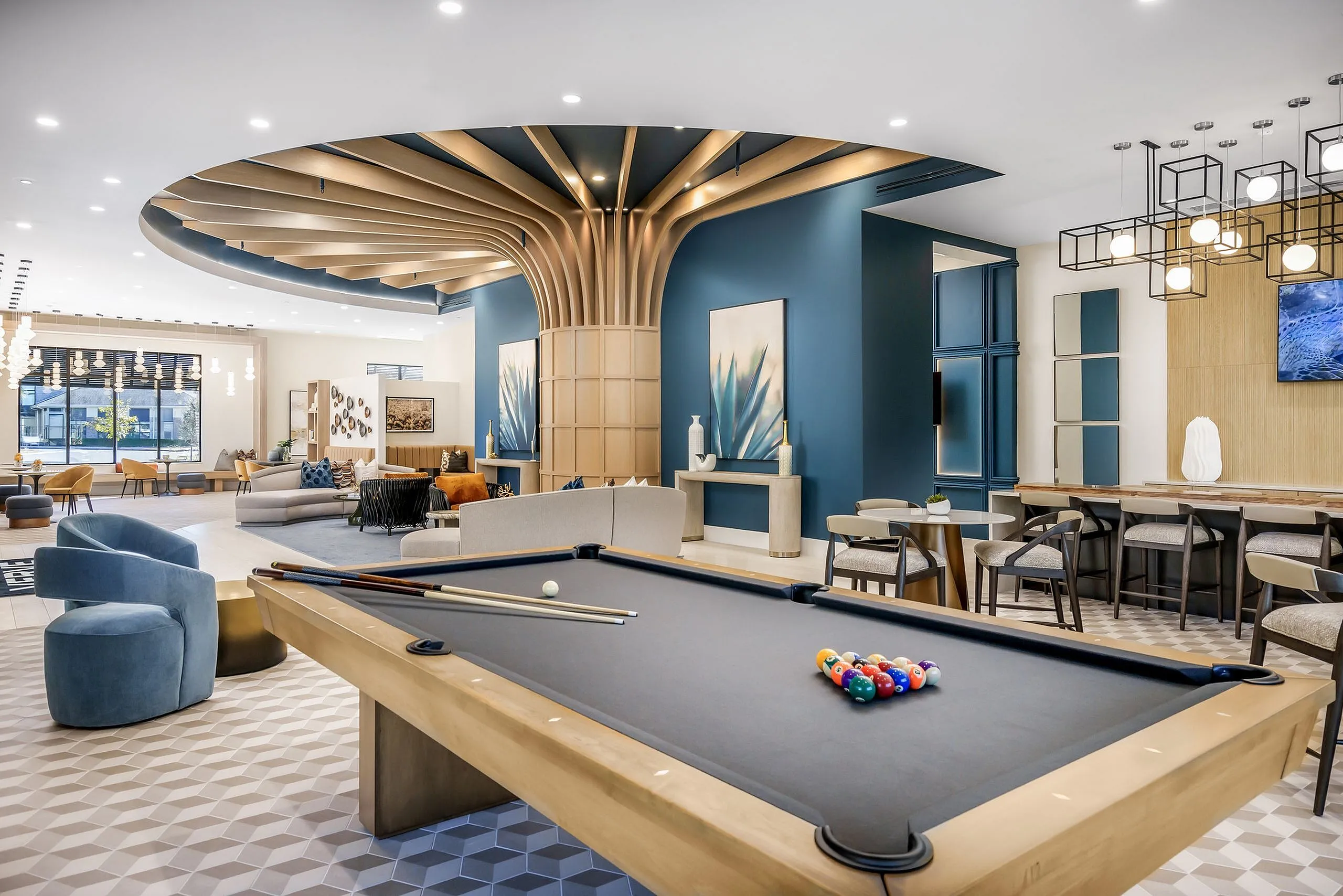 Elegant apartment lounge with modern decor, featuring a stylish pool table, plush seating, and ambient lighting under a unique, sculptural ceiling design.