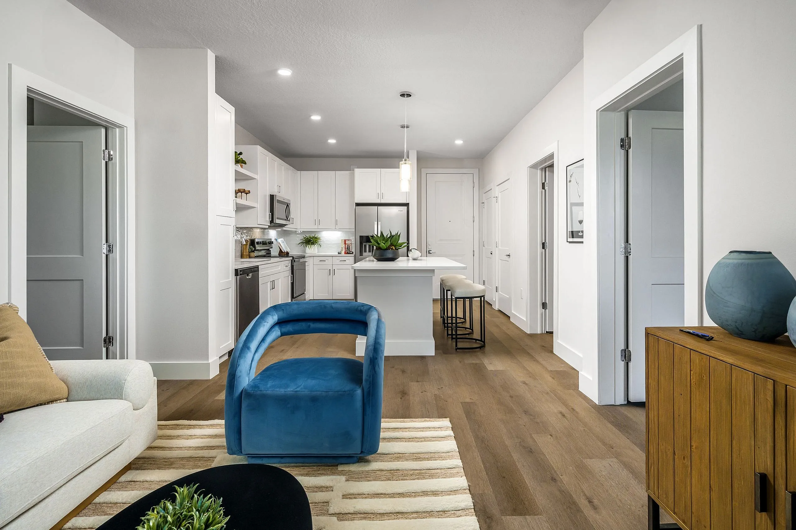 Modern open-concept living space featuring a sleek kitchen with stainless steel appliances, a cozy blue chair, and warm wooden flooring.