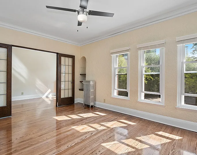 Bright and inviting living space with polished wooden floors, abundant natural light from large windows, and elegant French doors.