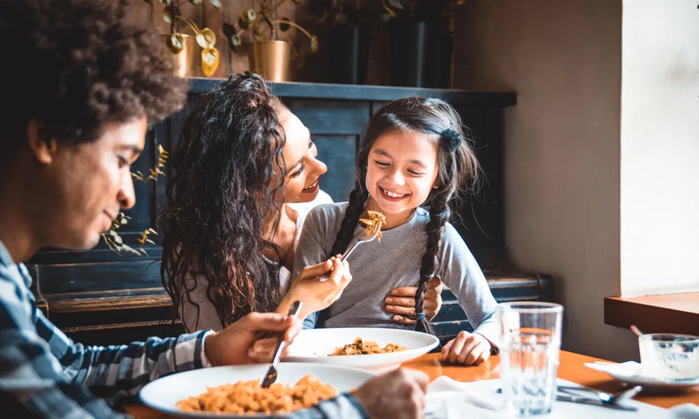 woman feeds child while man eats at same table at restaurant