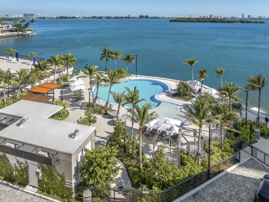 High-angle aerial view of Biscayne Shores overlooking the luxury pool deck and lush grounds toward the turquoise waters of Biscayne Bay.
