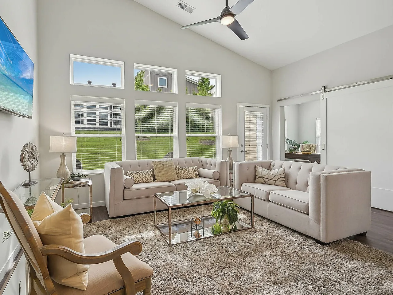 Elegant living room with plush beige sofas, large windows offering natural light, and a sleek modern ceiling fan.