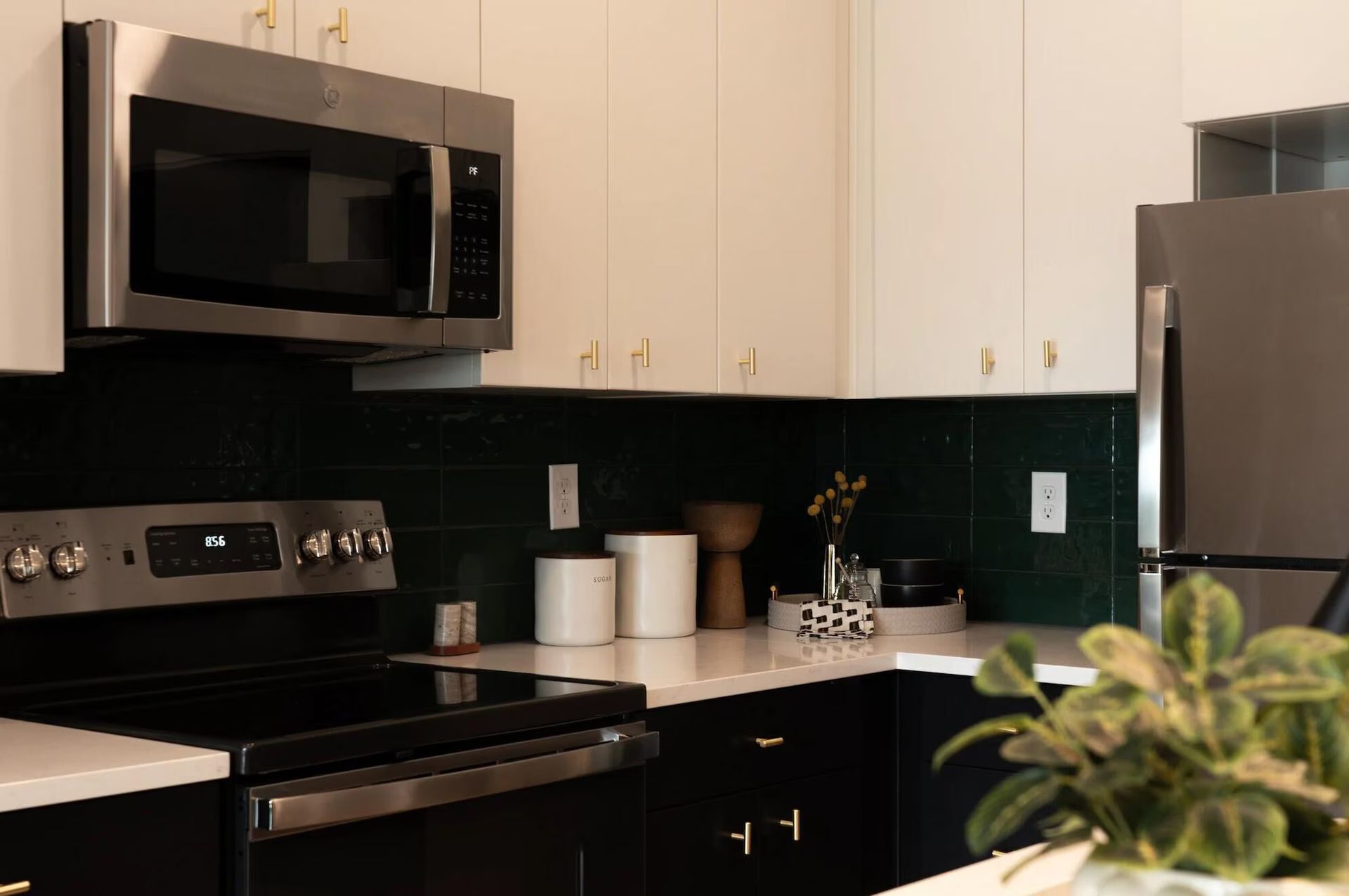 Modern kitchen with dark green tile backsplash, white countertops, and stainless steel appliances.