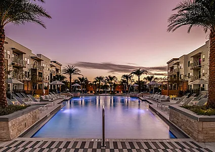 Luxurious apartment complex at sunset with palm trees and inviting resort-style pool.