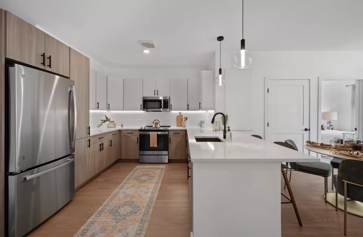 Modern kitchen with light and medium brown wood cabinets, pendant lights, and a dining area with green chairs.