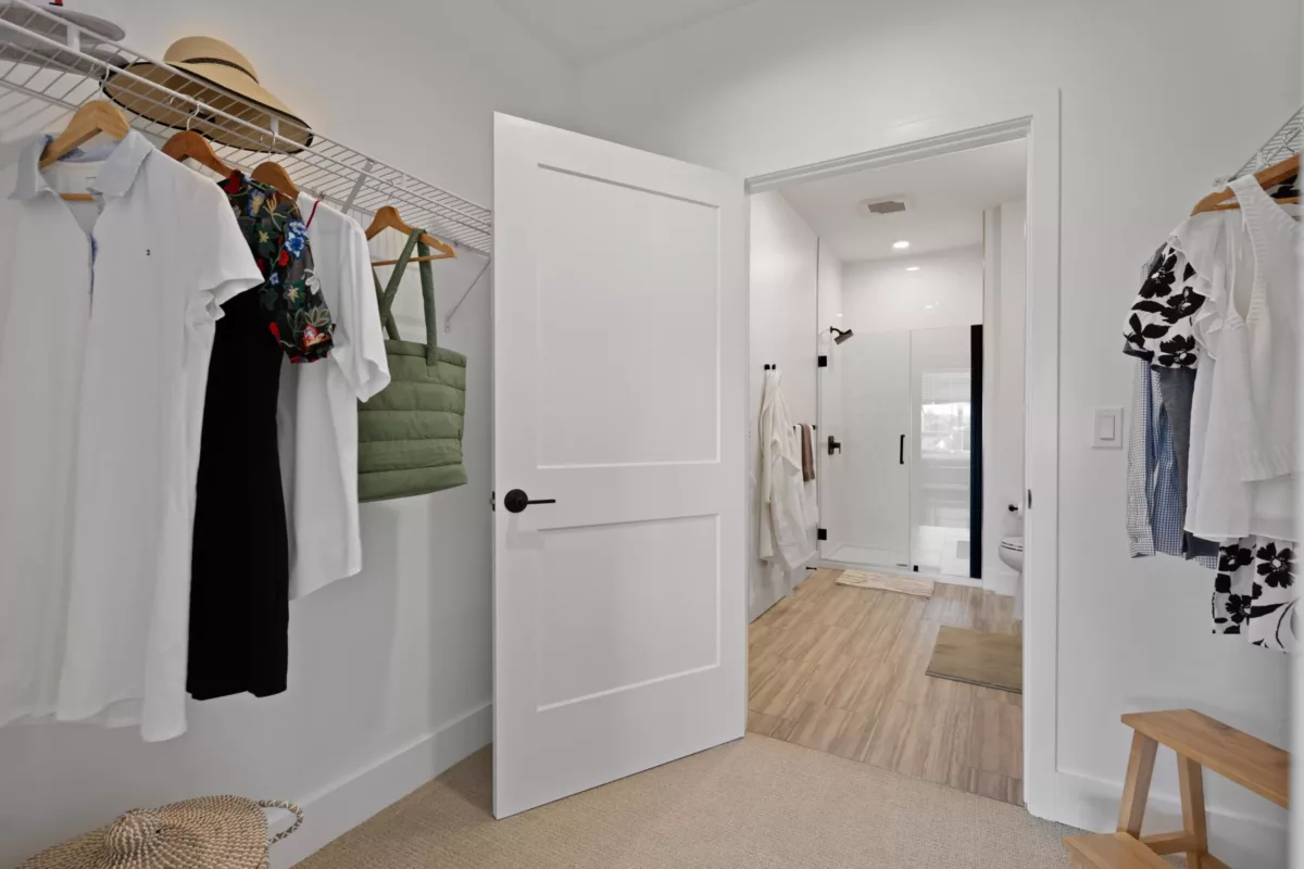 Oversized closet with clothes on hangers and an open door leading to the bathroom