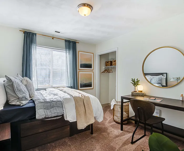 Bright and cozy bedroom featuring a plush bed, large window with elegant curtains, stylish desk, and a chic circular mirror.