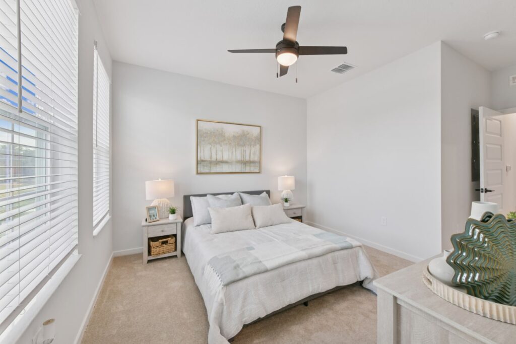 A bright bedroom at The Juliette features a neatly made bed, two side tables with lamps, a ceiling fan, and large windows flooding the space with natural light—perfect for your personal gallery of comfort and style.