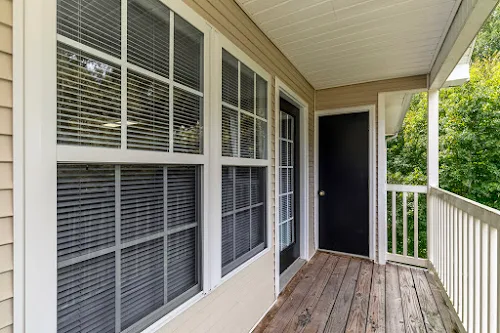 Balcony with wood plank flooring and white railing. View displays exterior of patio door and windows.