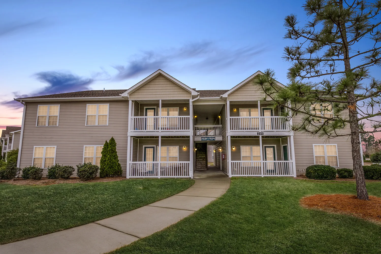Blue's Crossing apartment building with light brown siding surrounded by green space at dusk