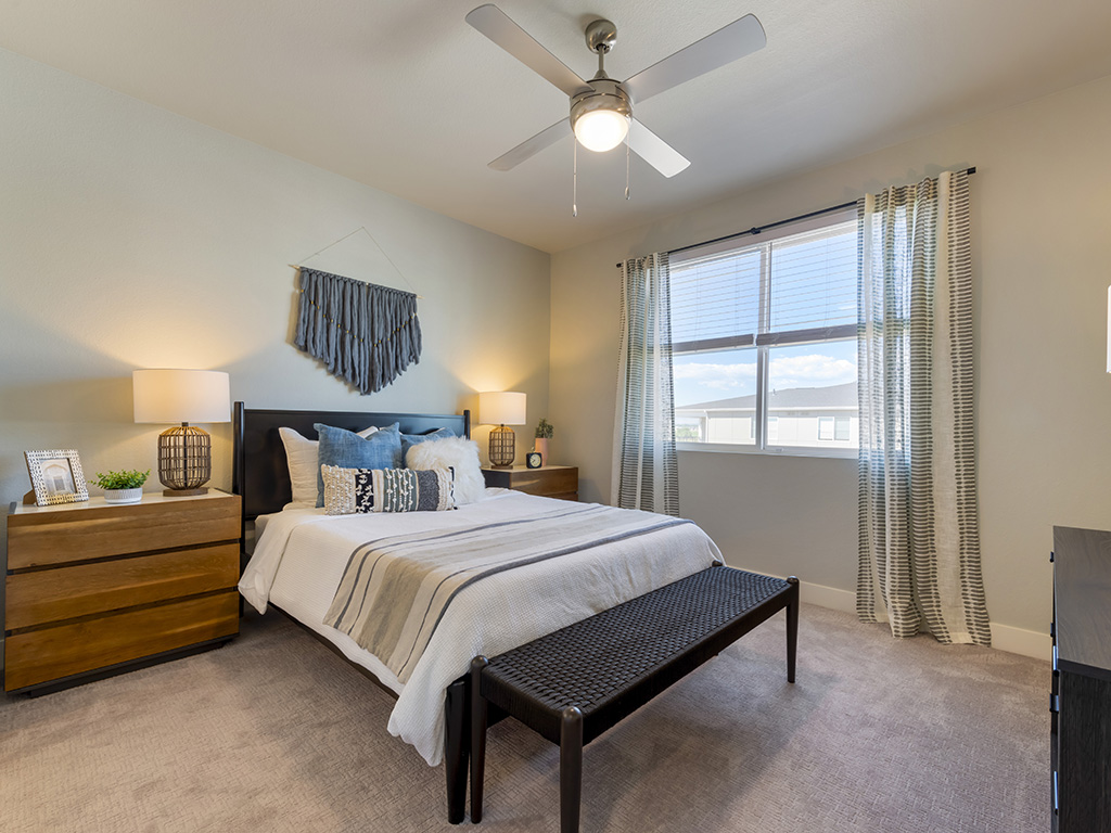 Bedroom with carpet, plush bed with headboard, bedside drawers with lamps, and large windows.