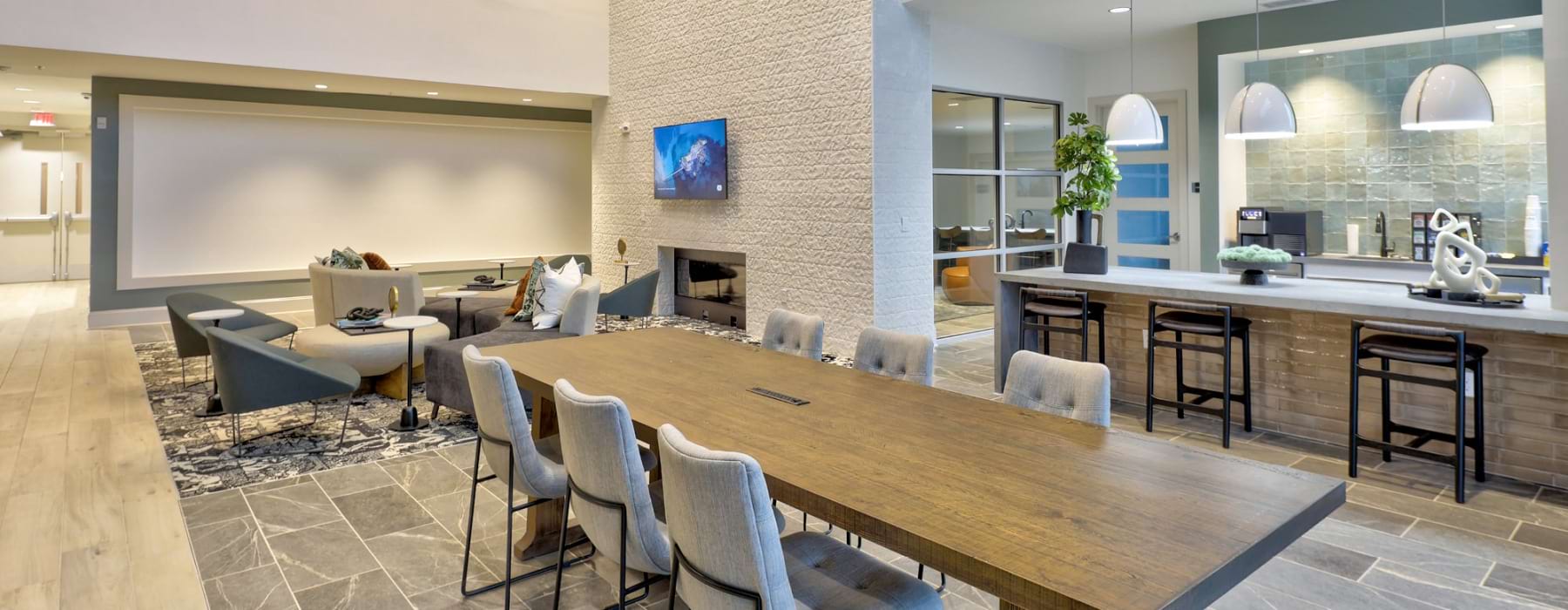 Clubhouse area at Mason with a large table and chairs, seating near the fireplace, and a high top bar island at our luxury apartments in Charlotte, NC.