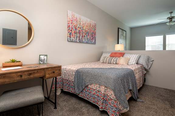 A bedroom with a bed, desk, chair, and a painting on the wall.