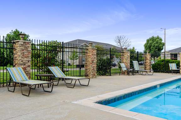 A pool area with lounge chairs and a black fence.