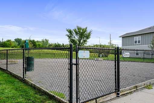 Lawrence, KS, Apartments for Rent - Remington Square - Dog Park with Gravel Ground, Pet Waste Station, Concrete Blocks, Landscaping, and Black Metal Fence.