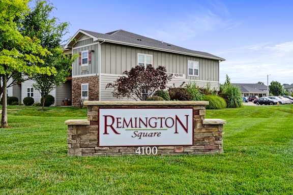 A sign for Remington Square with a house in the background.