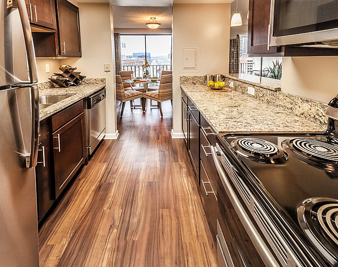 Chic modern kitchen with stainless steel appliances, elegant granite countertops, and a view leading to a bright dining area with cityscape sights.