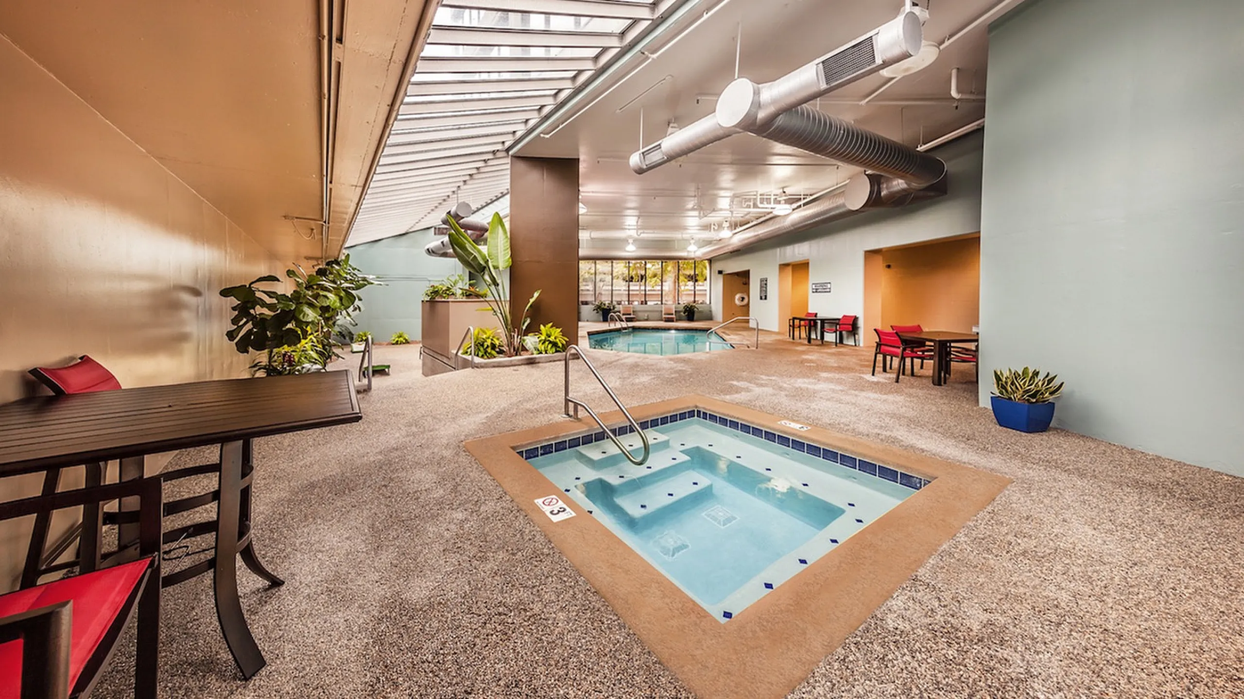 Luxurious indoor pool and spa area with skylights, modern seating, and vibrant greenery for a serene retreat.