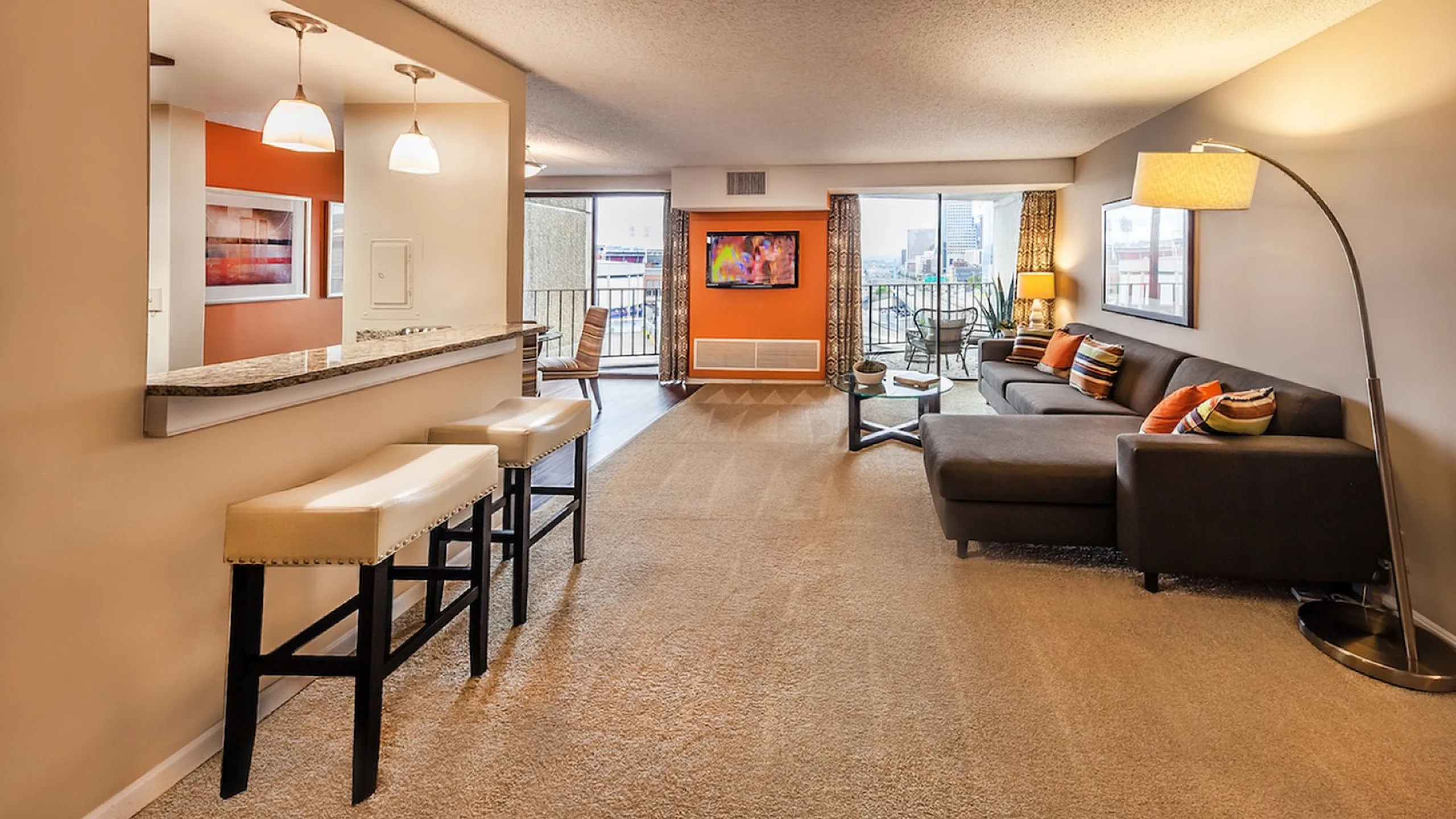 Bright open-concept living room with modern decor, featuring a chic sofa, stylish bar stools, and a scenic balcony view.