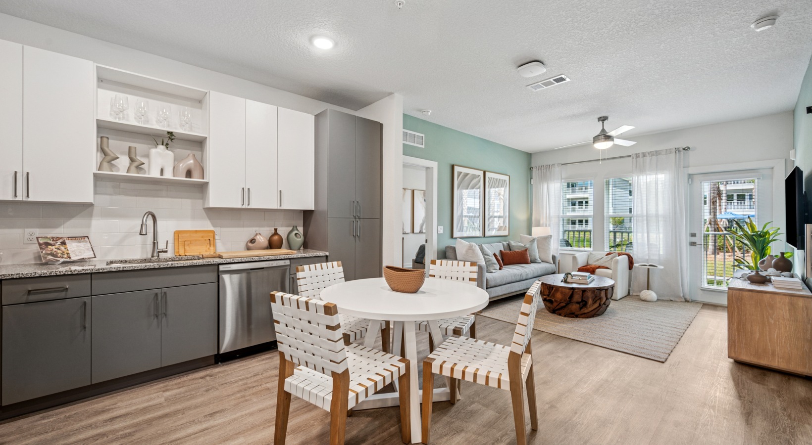 Modern open-concept apartment interior at Momentum Blanding featuring a dining area, stylish kitchen with white and gray cabinetry, and a bright living room with large windows.