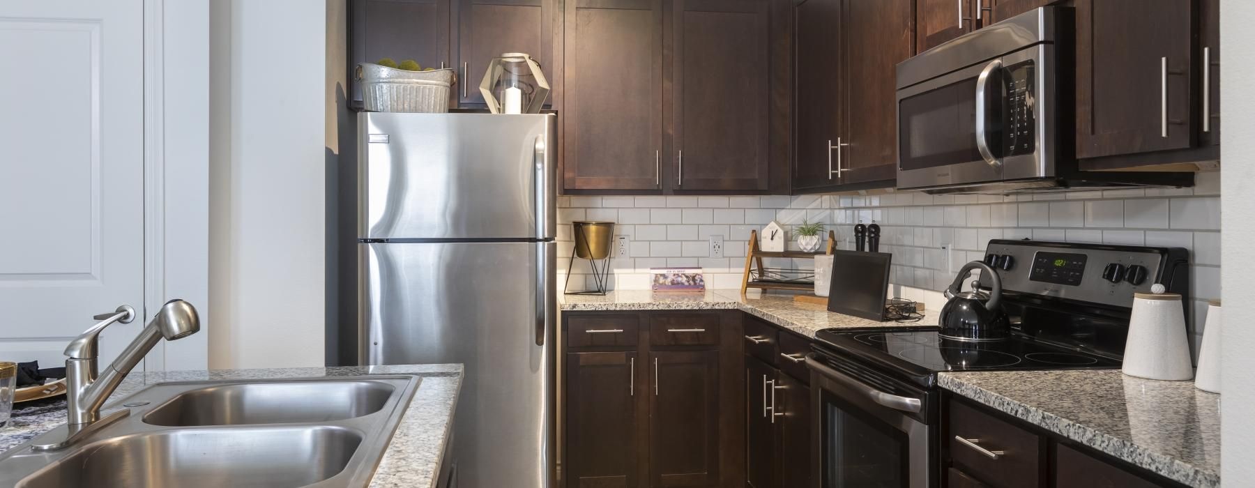 A kitchen with stainless steel appliances and dark wood cabinets at 4 Corners apartments in Frisco, TX