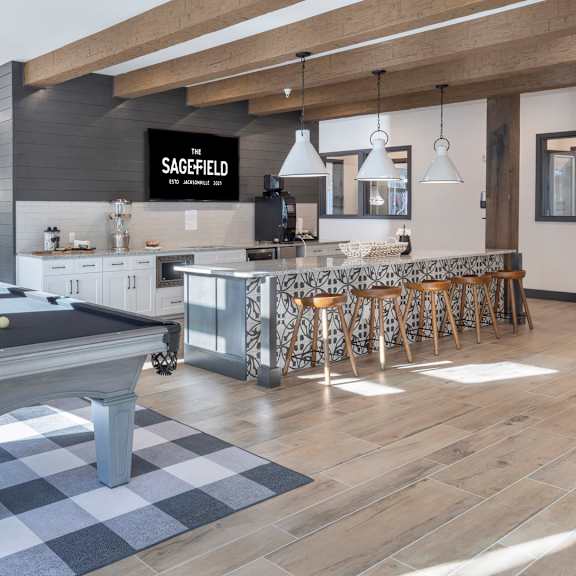 A pool table is in the middle of a room with a kitchen in the background.