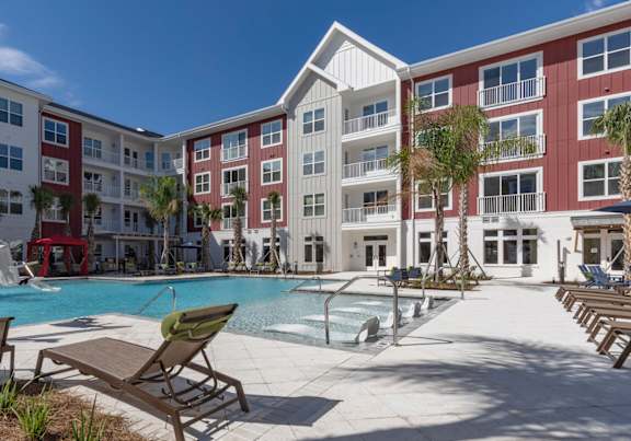 A pool area with lounge chairs and a fountain in front of apartment buildings.