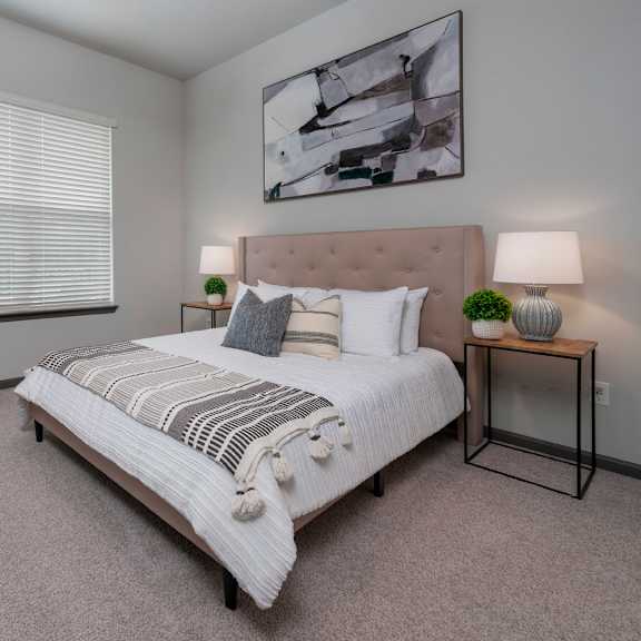 A bedroom with a large bed, a nightstand, and a plant on a dresser.
