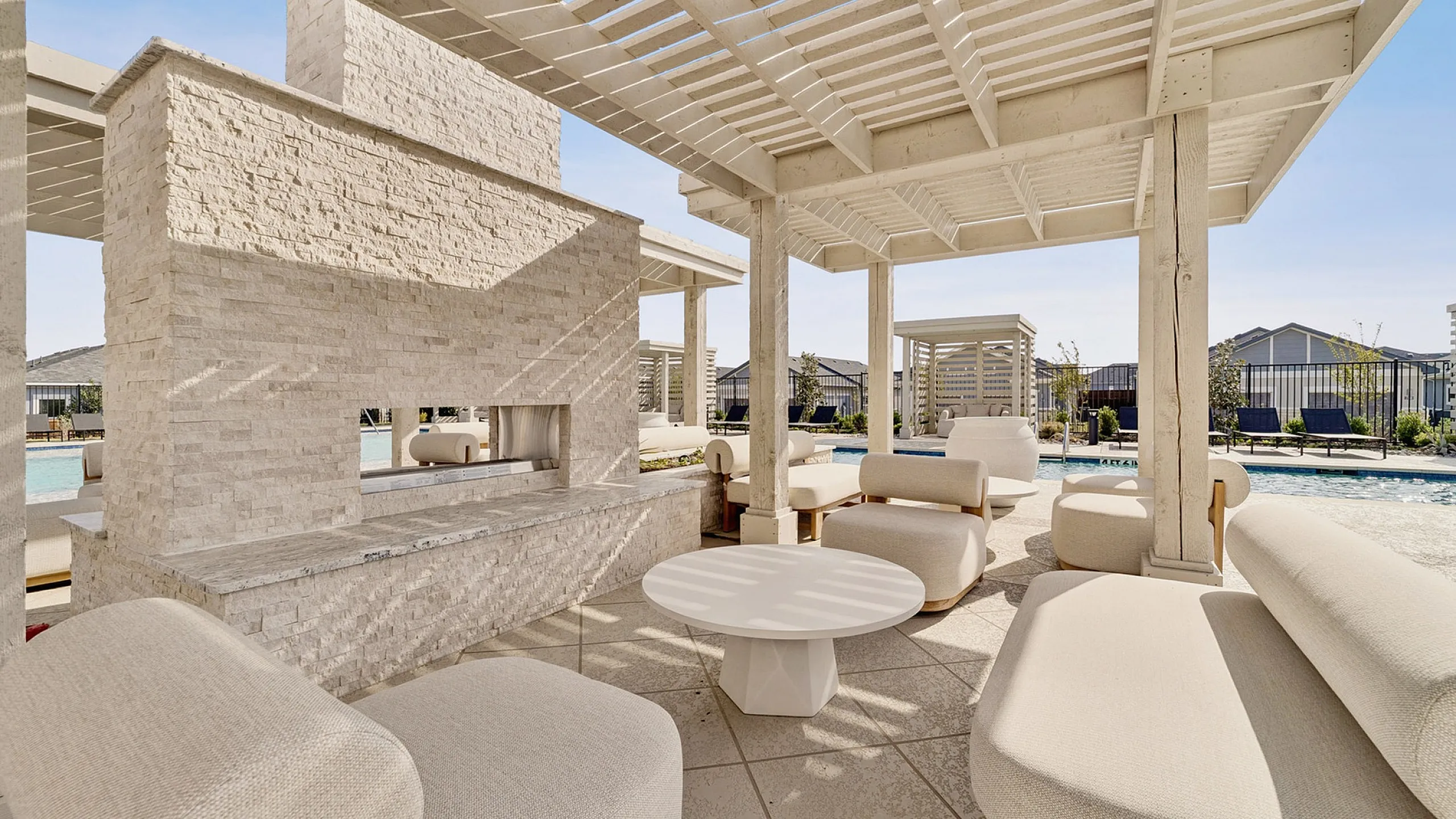 Luxurious outdoor lounge area with elegant white furnishings, shaded pergola, and poolside views.