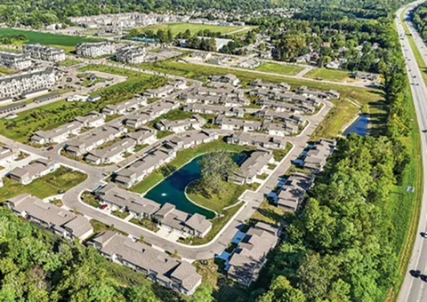 Stunning aerial view of a modern suburban community featuring winding streets, lush greenery, and a serene central pond, offering a peaceful living experience.