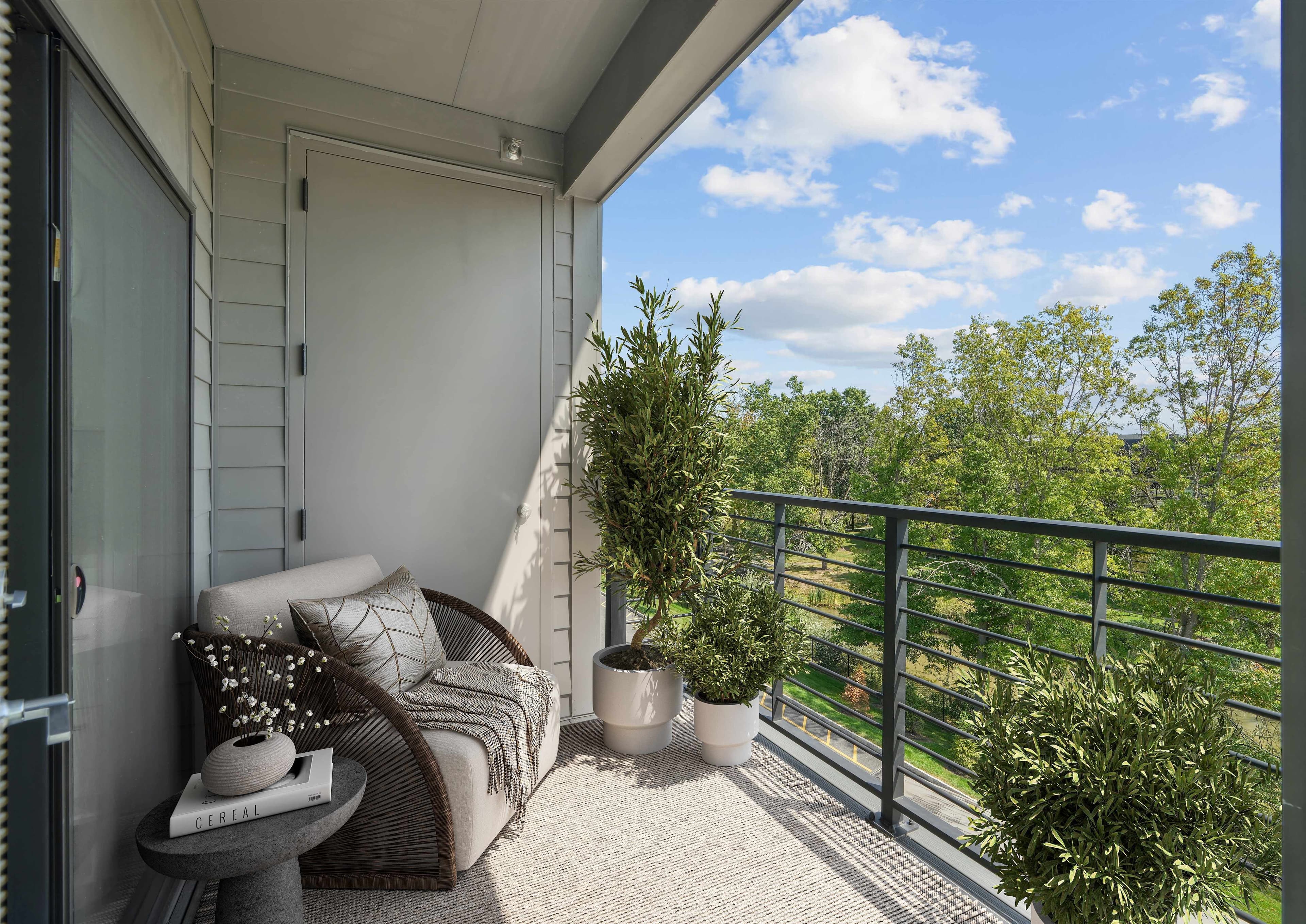 Private apartment balcony with a lounge chair, potted plants, and scenic tree views at Livana East Hanover in New Jersey