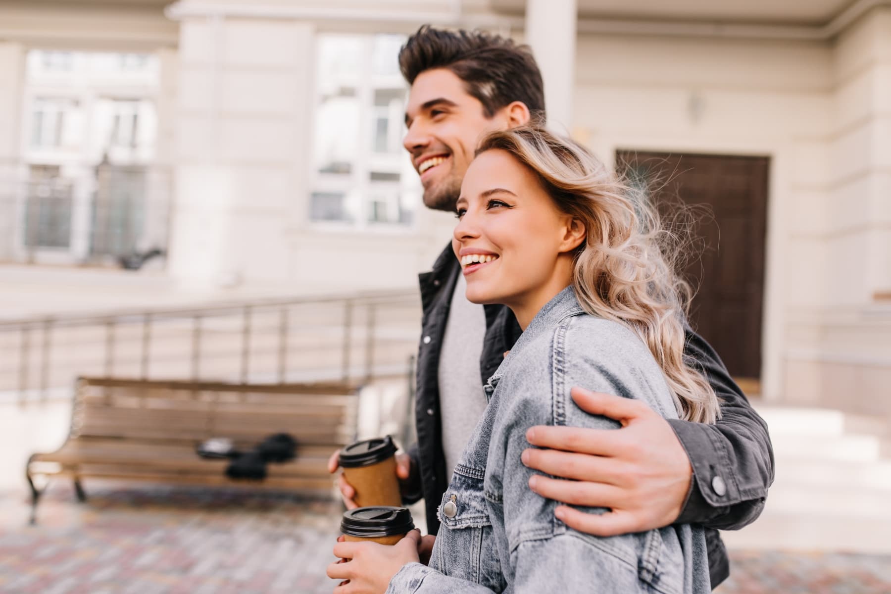 Smiling couple walking outdoors with coffee cups, enjoying a sunny day at Livana East Hanover in New Jersey.