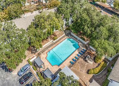 An aerial view of a swimming pool surrounded by trees and a parking lot.