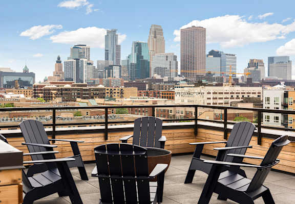 A balcony with black chairs and a table overlooking a city skyline.