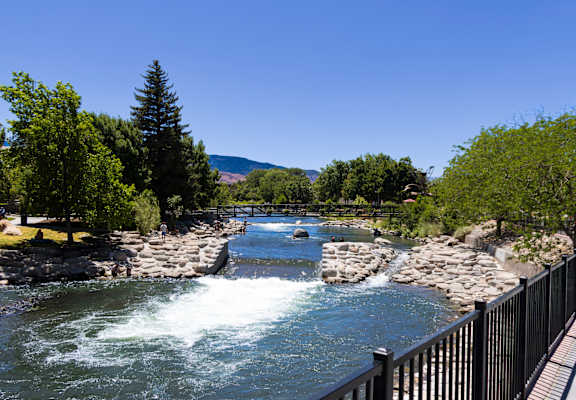 Close-up of a rustic metal bridge with hanging baskets of purple and pink flowers over the river at ONE18 West Street Residential Apartments, Nevada