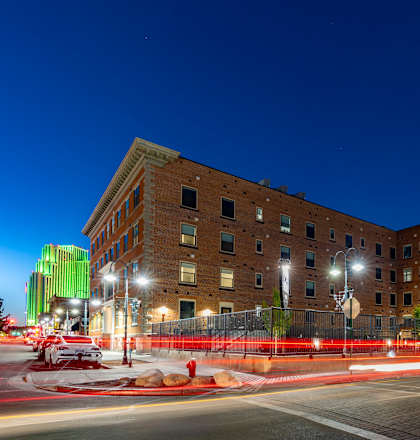 A city street at night with a large building in the background and a red fence in the foreground.
