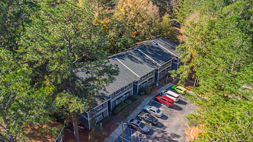 A parking lot with a building and cars is surrounded by trees.