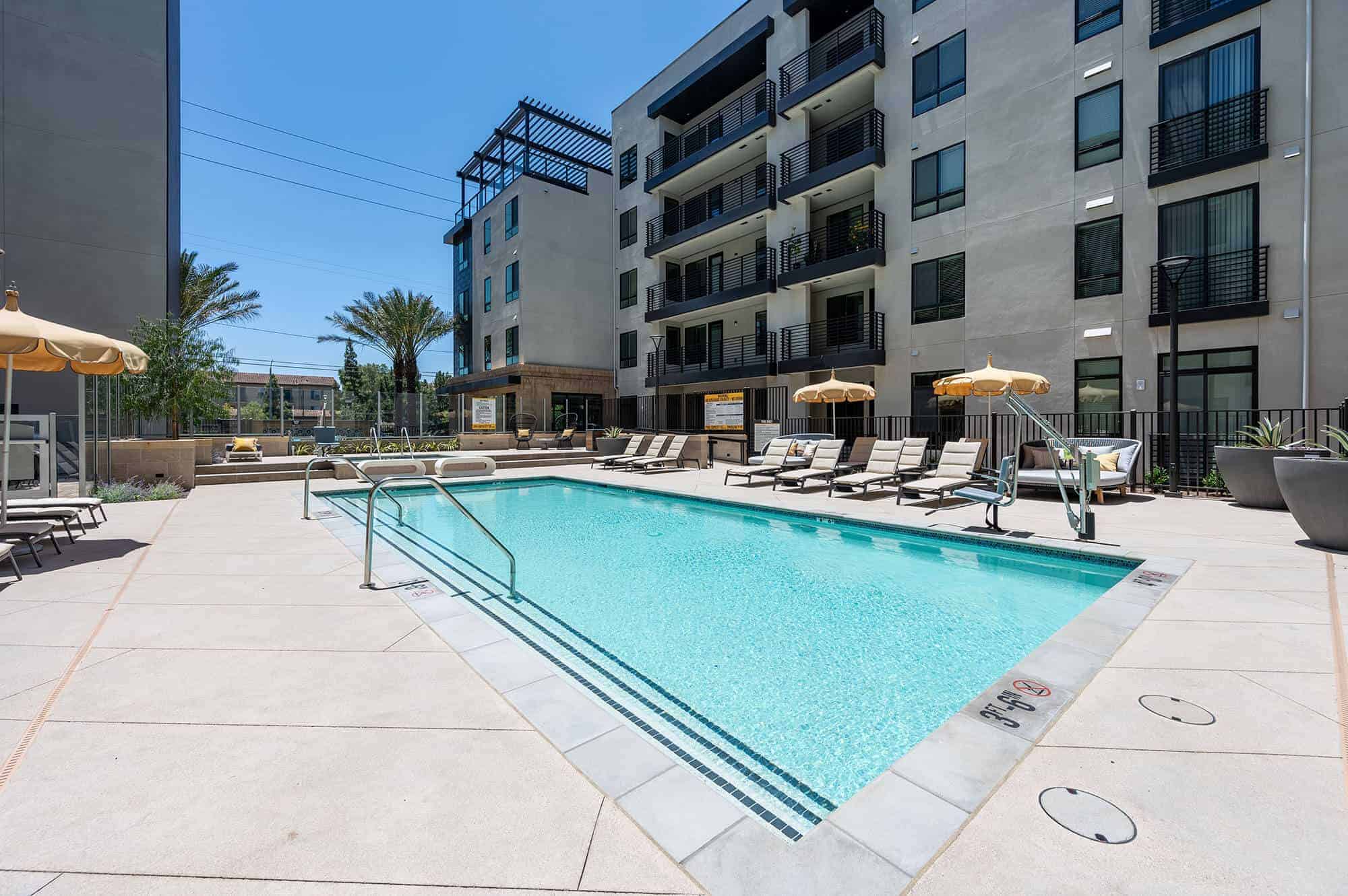Wide outdoor pool with lounge chair and umbrellas.
