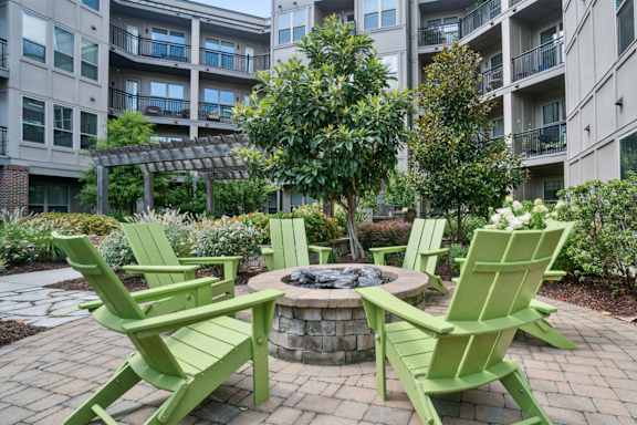 A fire pit surrounded by green chairs in a courtyard at The Linden Apartments, Davidson, NC